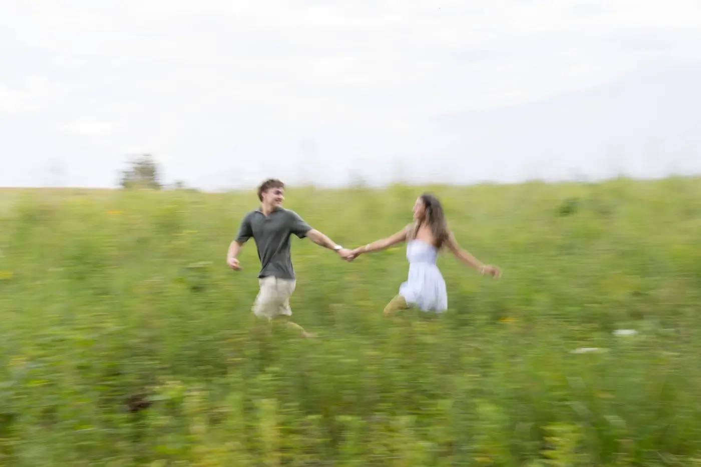 A couple running hand in hand through a green field during an engagement session