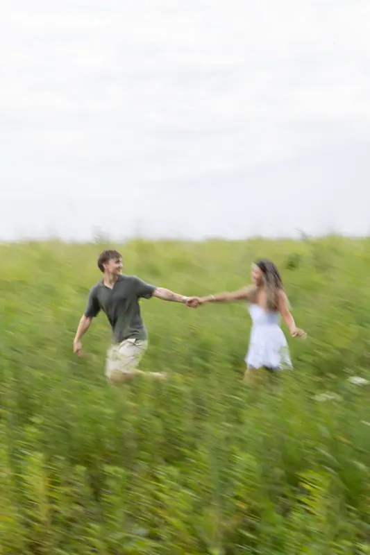 A couple running hand in hand through tall green grass, caught with motion blur