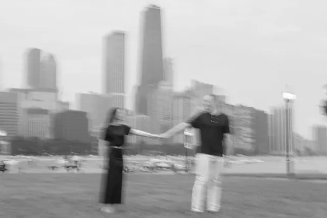 A couple holding hands on the lakefront grass with the Chicago skyline behind them, photographed in black and white with motion blur