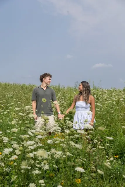 A couple holding hands in a field of white wildflowers, looking at each other