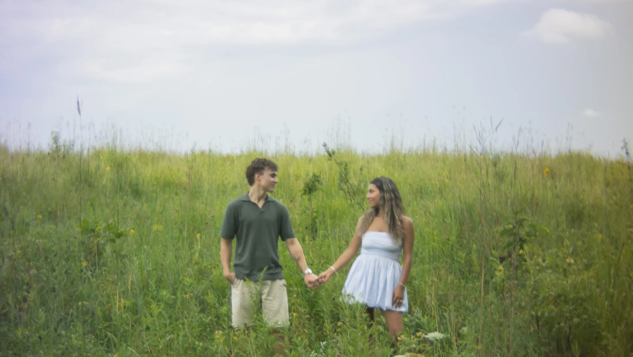 A couple walking into a wildflower meadow under a heavy violet sky