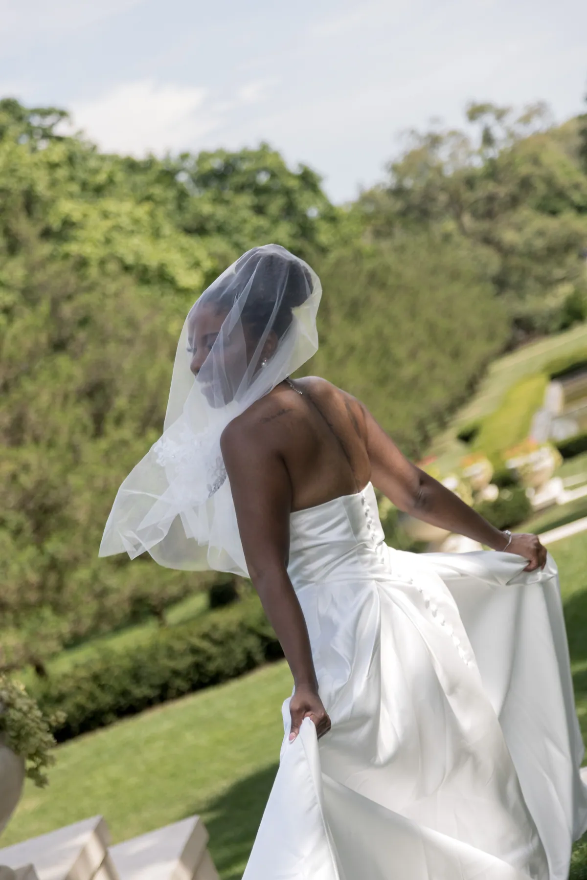 A bride walking away down a clipped hedge path, her veil lifting behind her