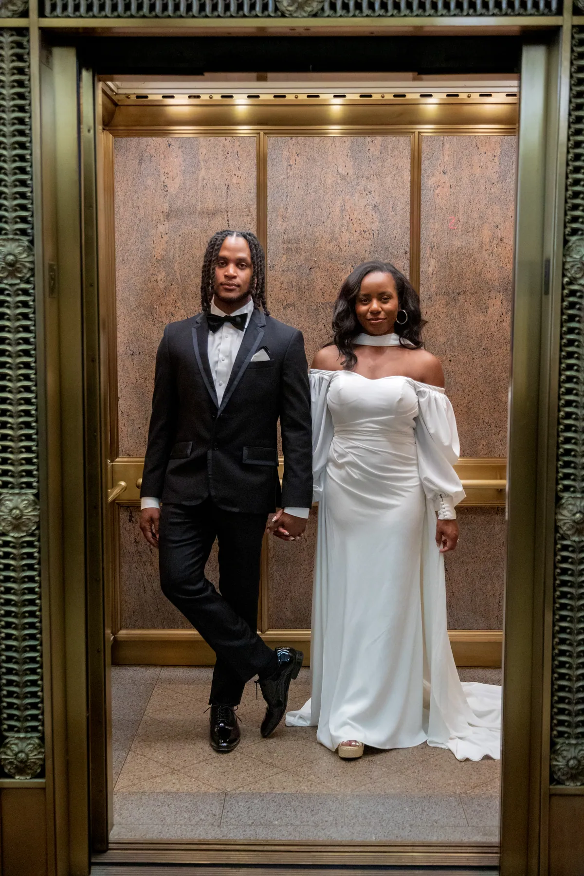 A couple standing together in a brass lift with the doors open