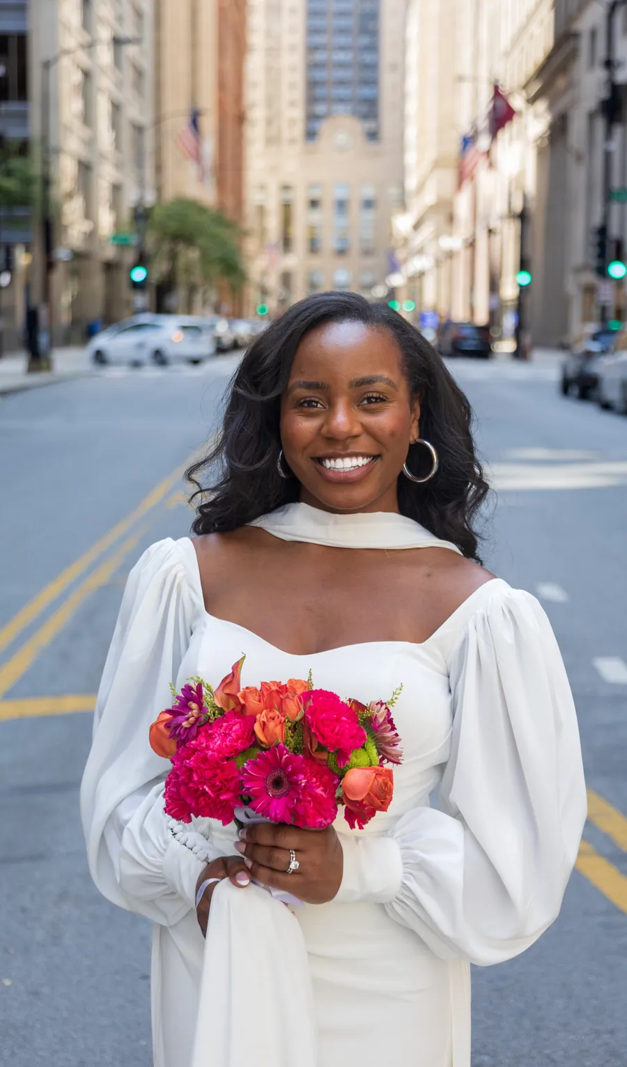 A bride on a downtown street holding a bouquet of hot pink and red blooms