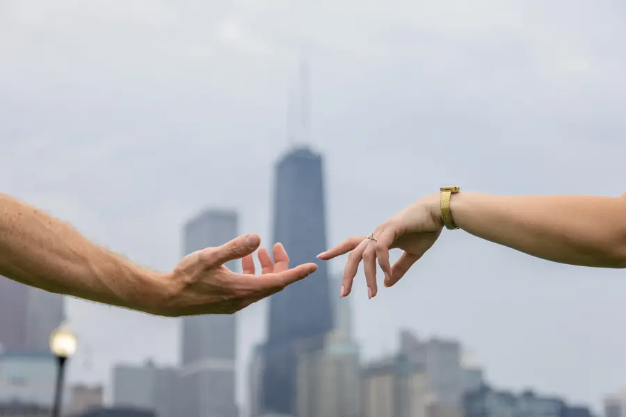 Two hands reaching for each other in front of the John Hancock Center