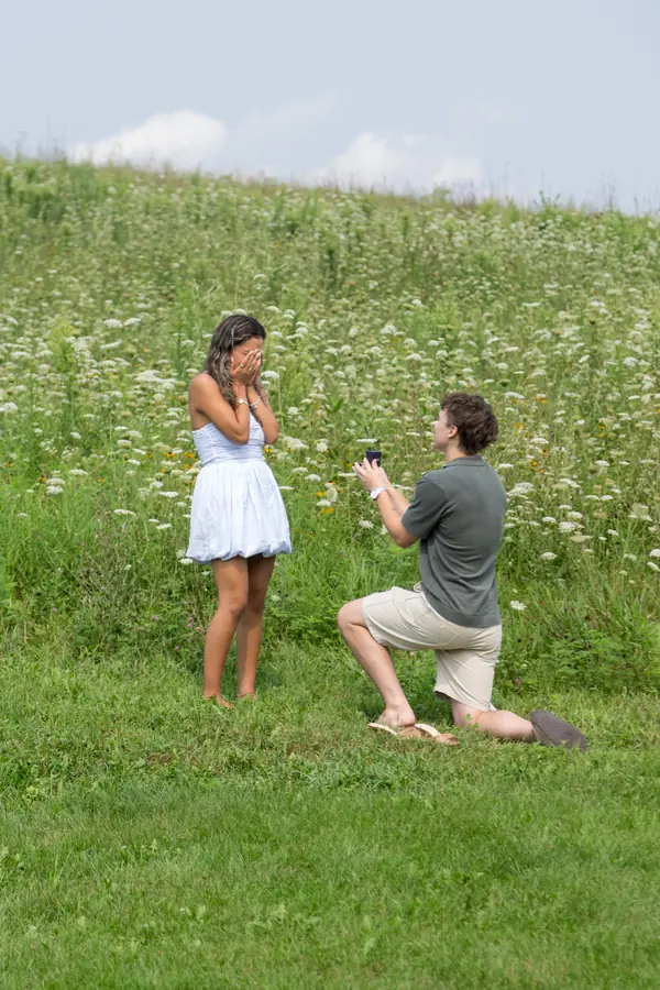A man down on one knee proposing in a hillside meadow