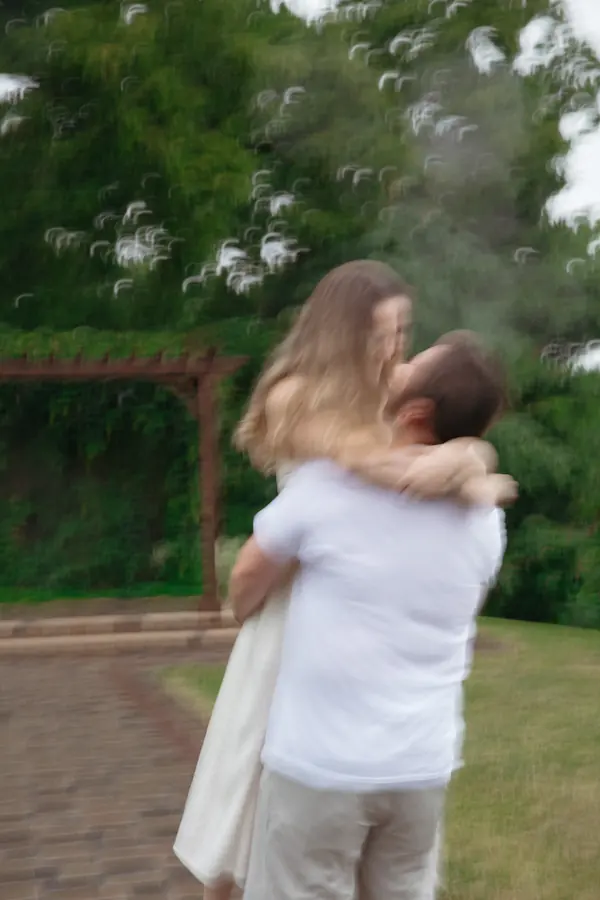 A man spinning his partner in his arms beside a garden pergola