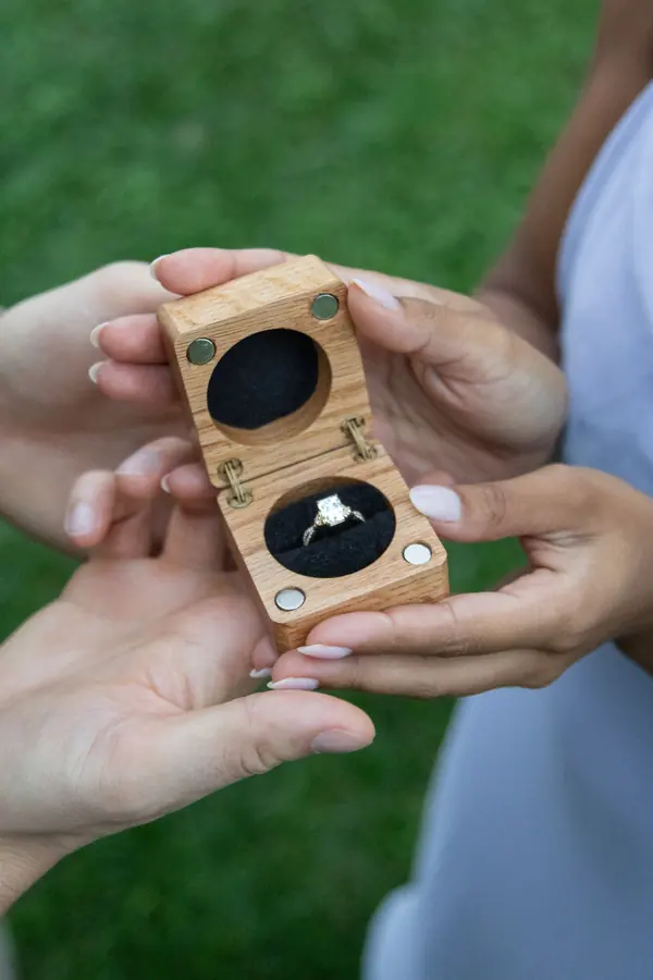 An engagement ring in an open wooden box held in two hands