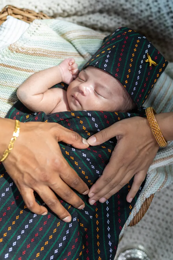 A newborn swaddled in a striped blanket in his parent's hands