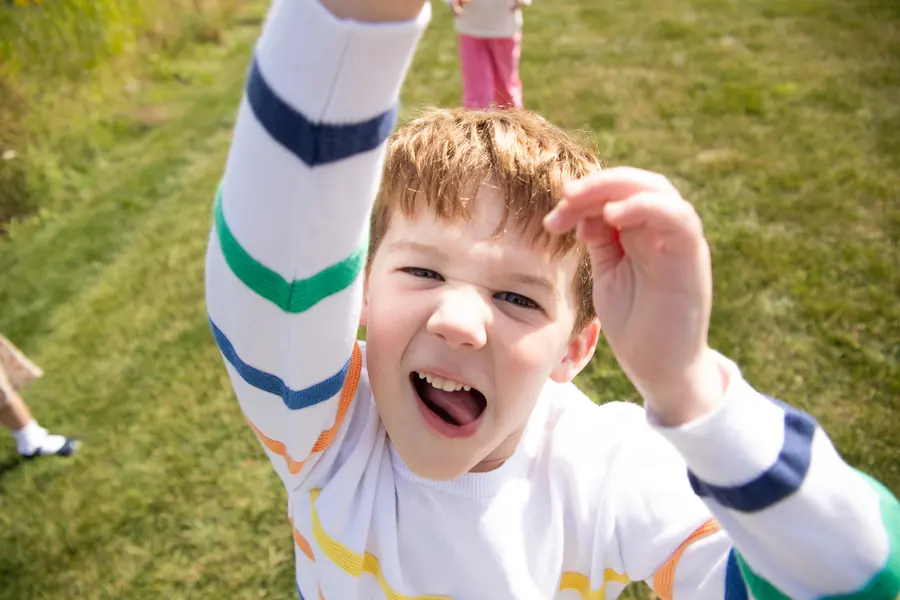 A little boy reaching up toward the camera with a big grin