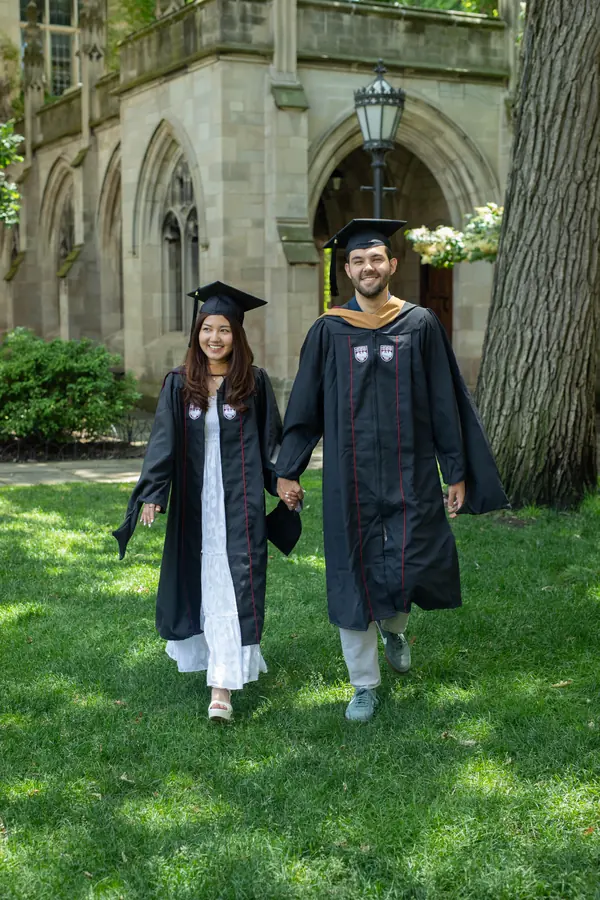 Two graduates walking across a campus lawn in their gowns
