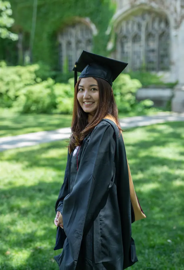 A graduate smiling on campus in her gown
