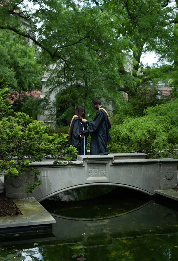 Two graduates standing on a stone bridge over a pond