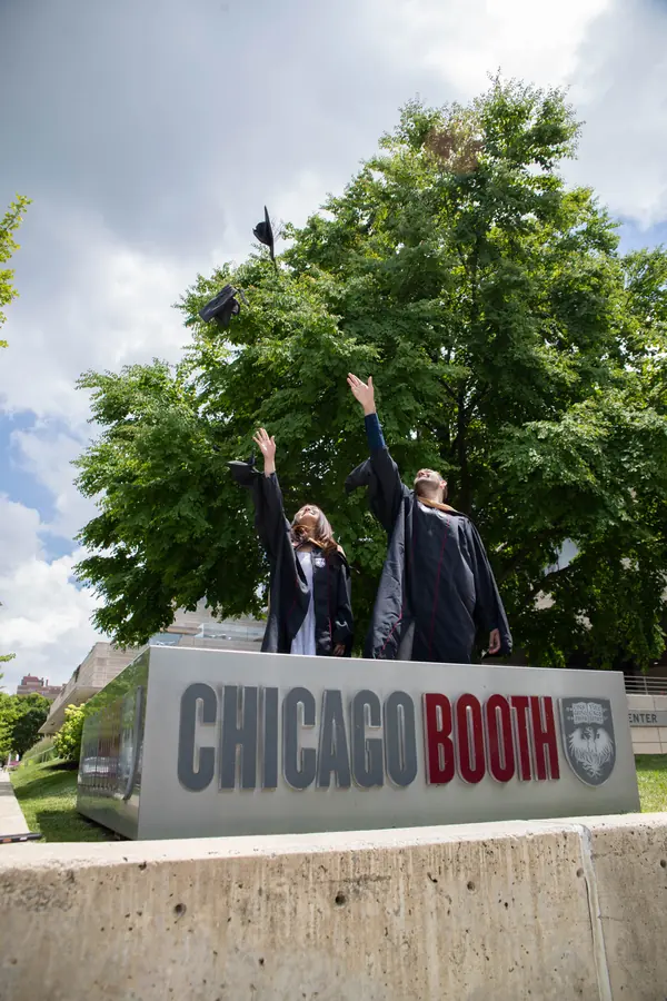 Graduates throwing their caps behind the Chicago Booth sign