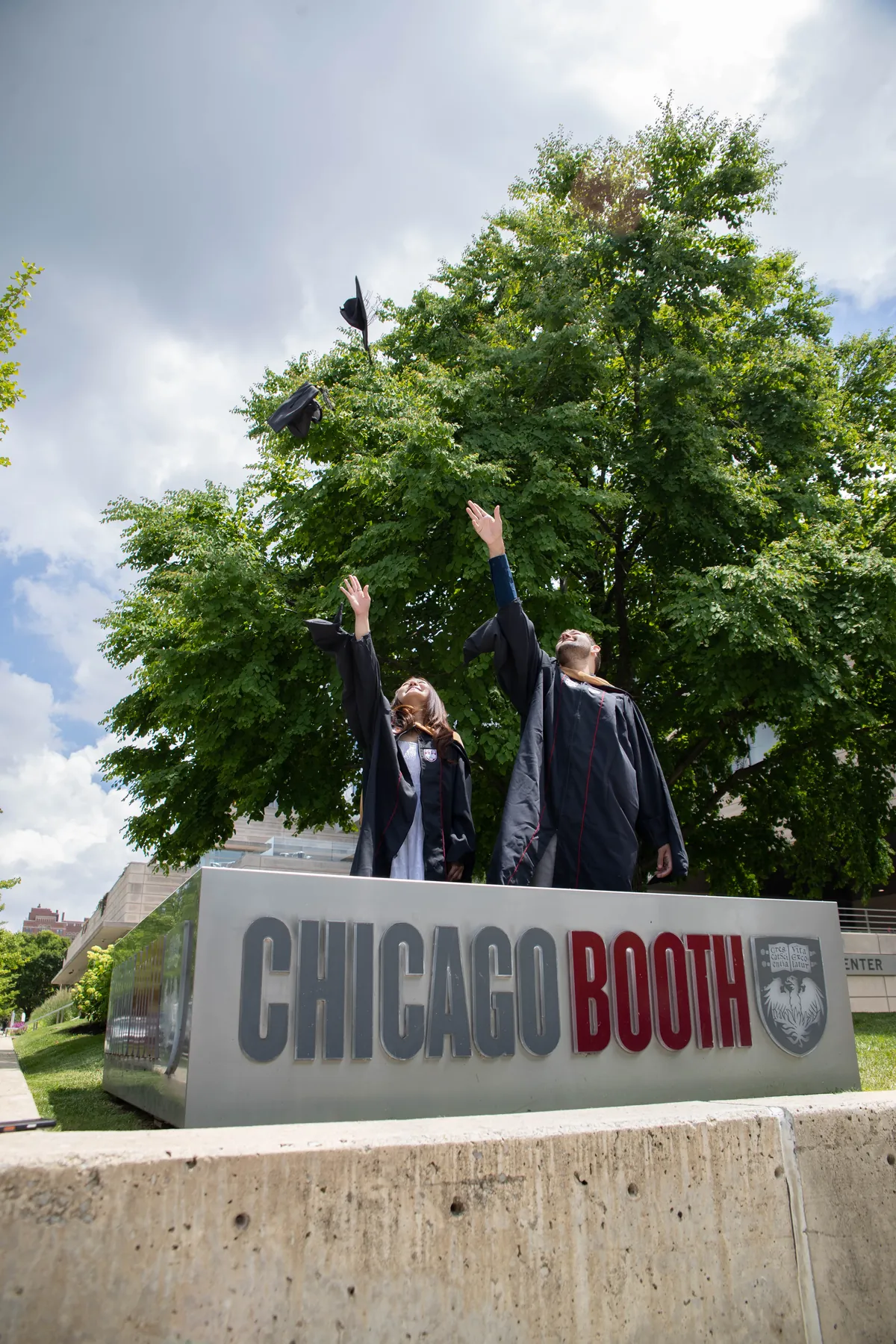 Graduates throwing their caps behind the Chicago Booth sign