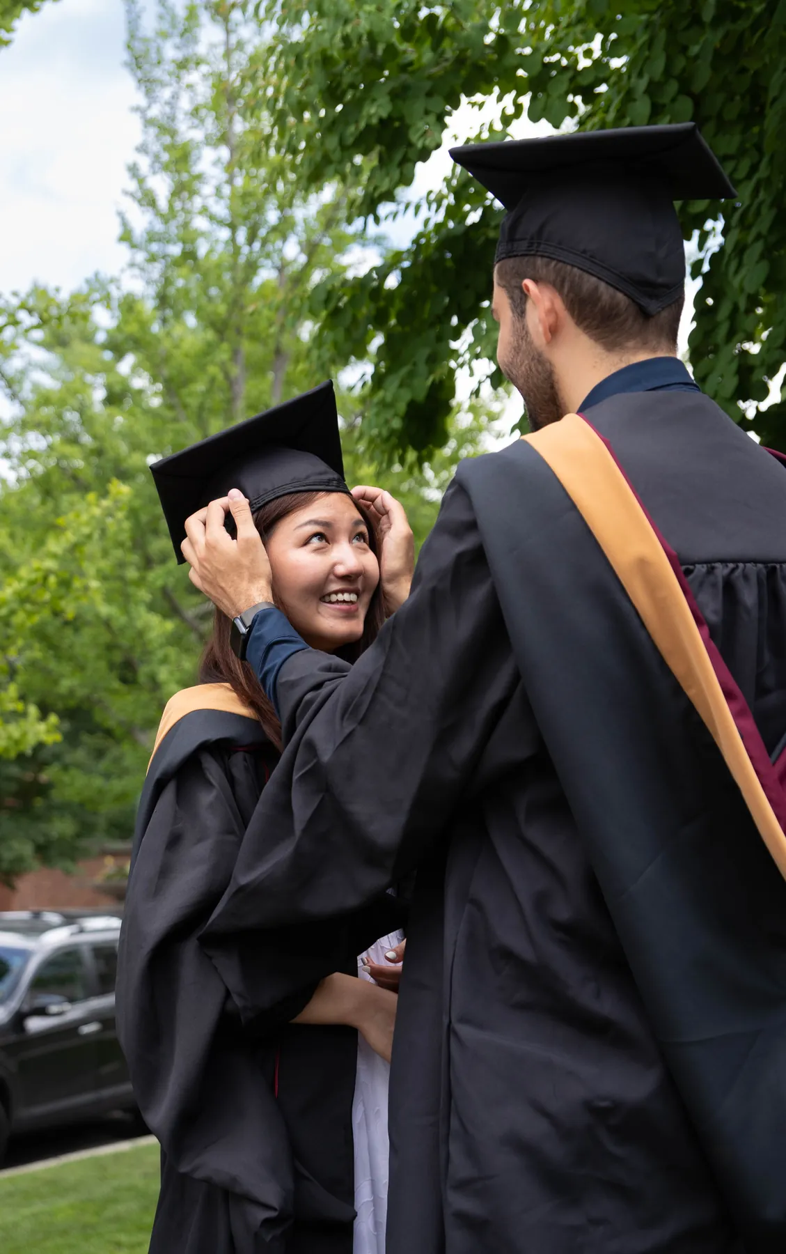 A graduate hugging her classmate beneath the trees