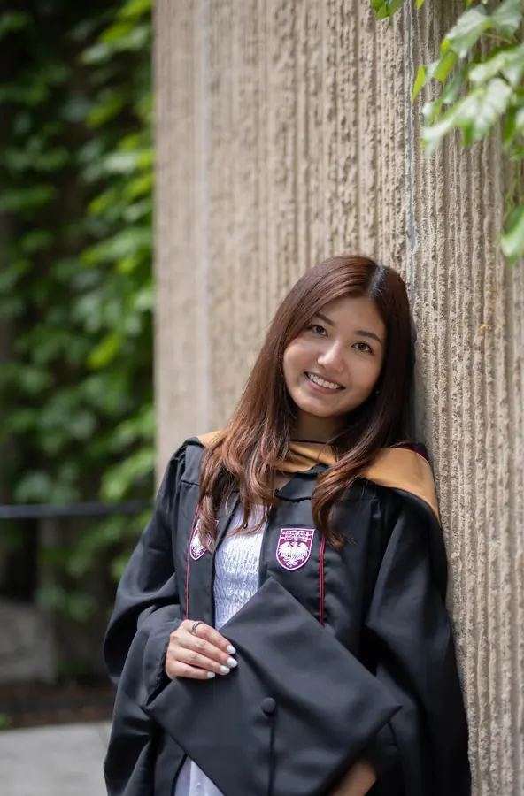 A graduate leaning against a stone column holding her cap