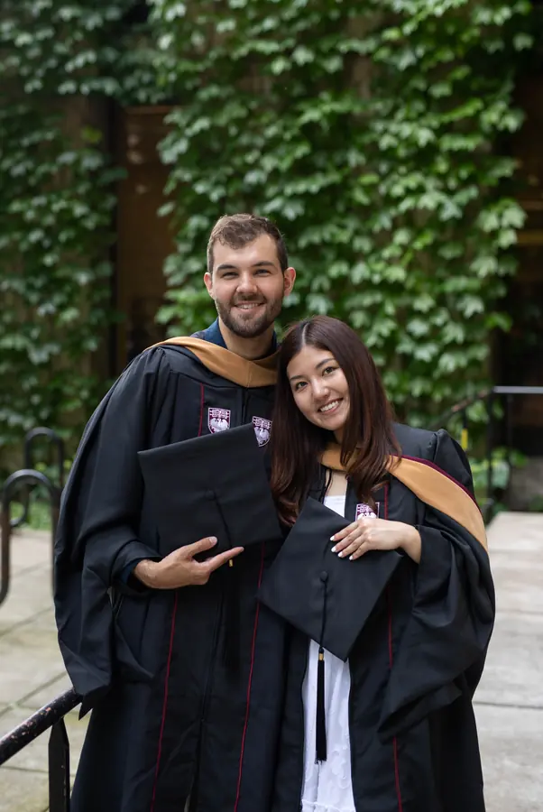 Two graduates smiling in front of an ivy wall