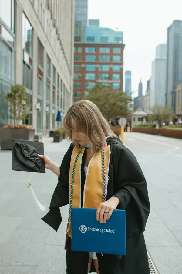 A graduate holding her diploma cover on a downtown sidewalk