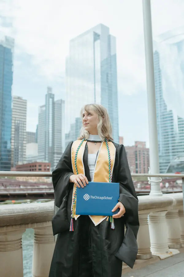 A graduate standing against the glass towers along the river
