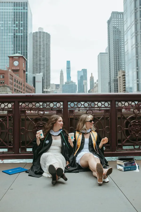 Two graduates sitting on the bridge with books and coffee