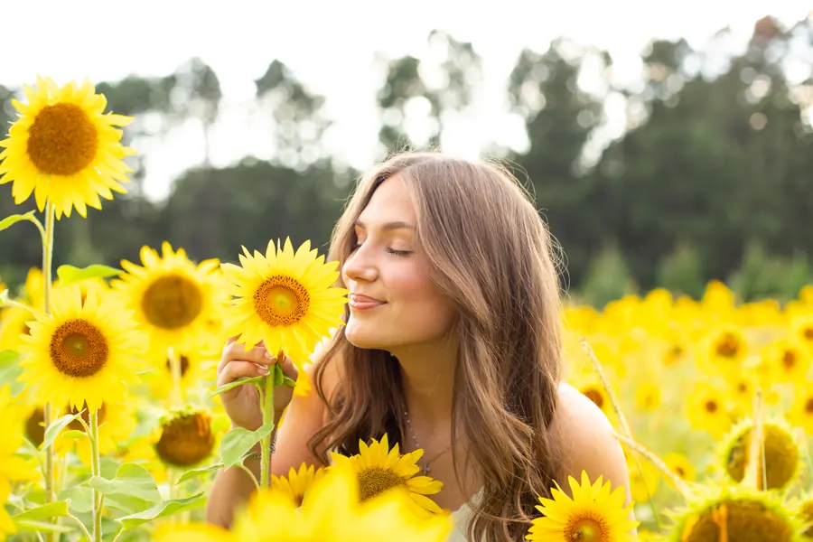 A senior smelling a sunflower in a sunlit field