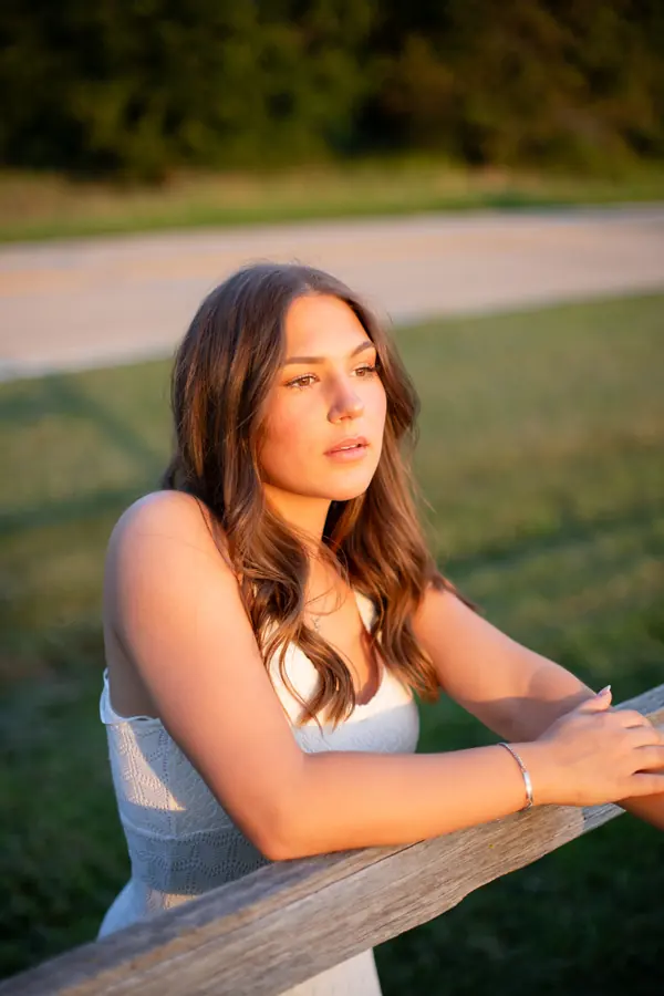 A senior leaning on a wooden fence at golden hour