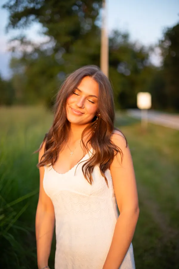A senior in a white dress standing in warm evening light