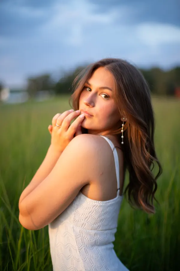A senior posing in a green field under a blue sky