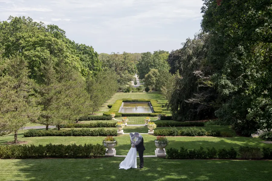 A bride and groom in the middle of a long formal garden