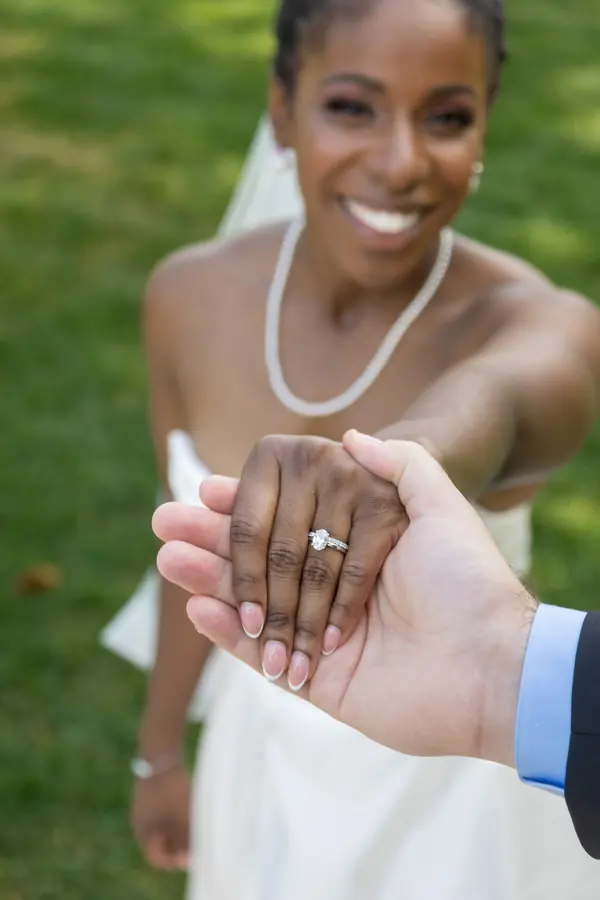 A bride smiling behind her groom's hand and wedding ring