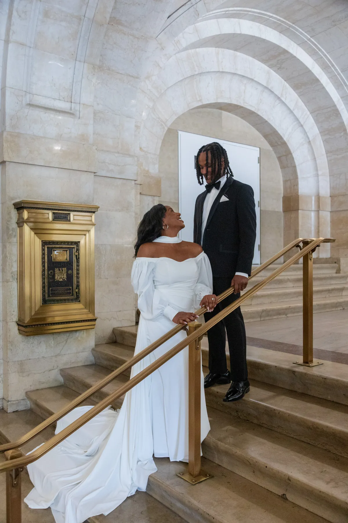 A bride and groom on a marble staircase under a stone arch