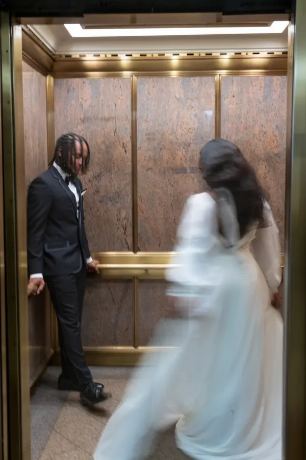 A bride sweeping past her groom in a brass elevator, caught in motion