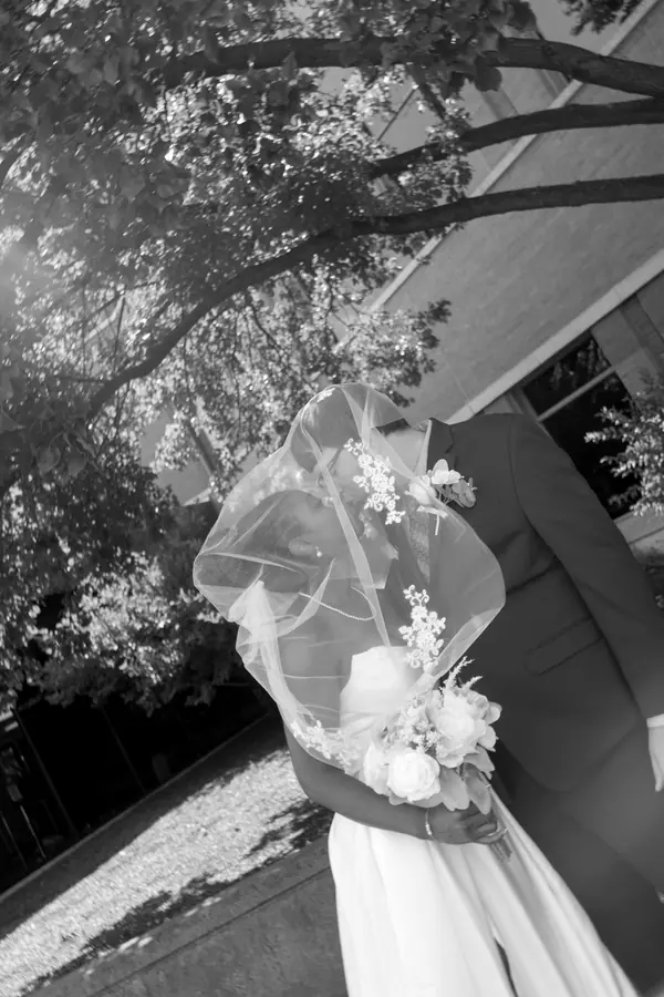 Black and white: the bride under the pergola holding her bouquet low
