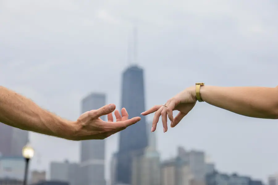 Two hands reaching toward each other, the skyline soft and out of focus between them