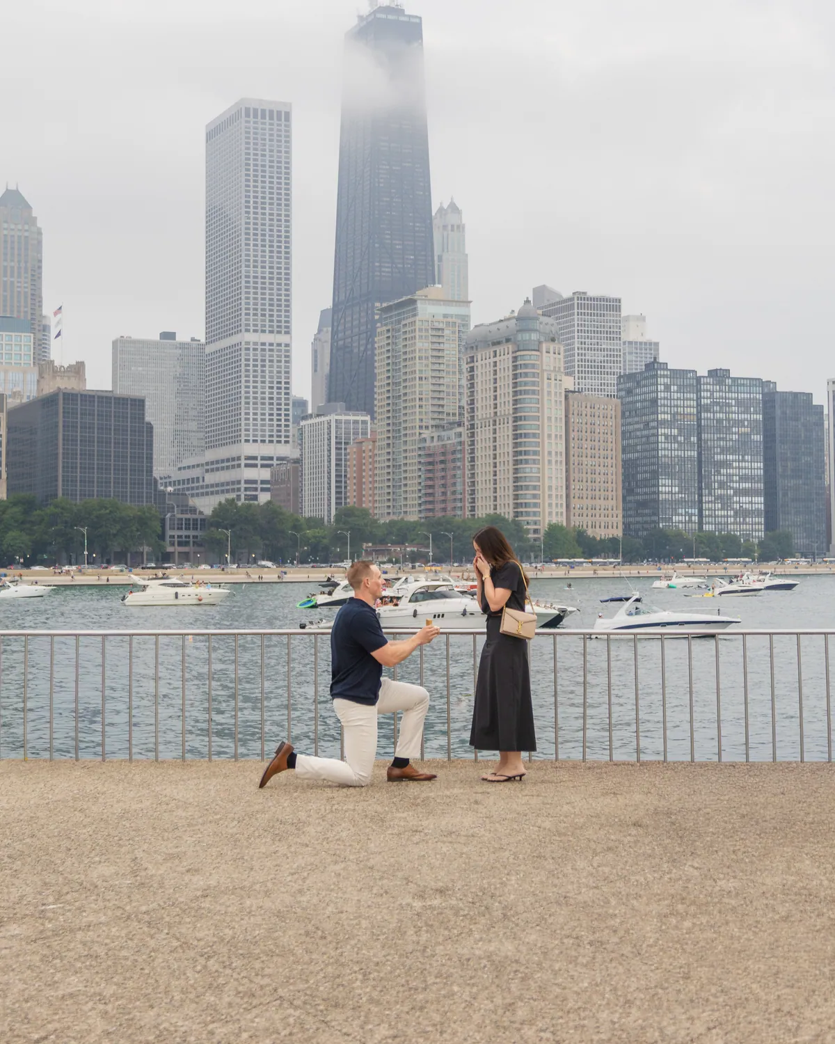 The proposal itself: he is down on one knee on the path, the Chicago skyline and the lake filling the frame behind them