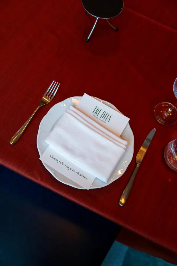 A place setting on a red cloth, gold rimmed plate, folded menu card and cut glass