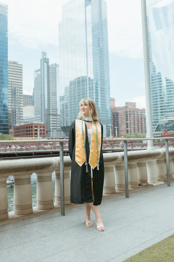 Standing at the bridge rail in cap and gown, the river running off into the city