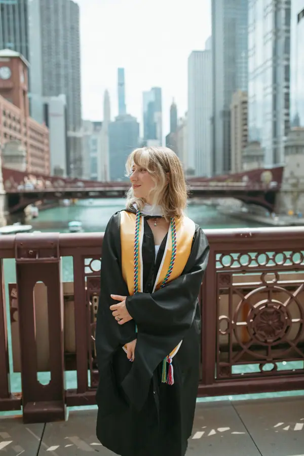 Leaning on the iron bridge rail in her hood and gown, downtown behind her