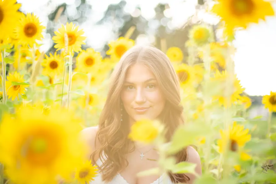 A close frame through the sunflower heads, her face catching the last of the light