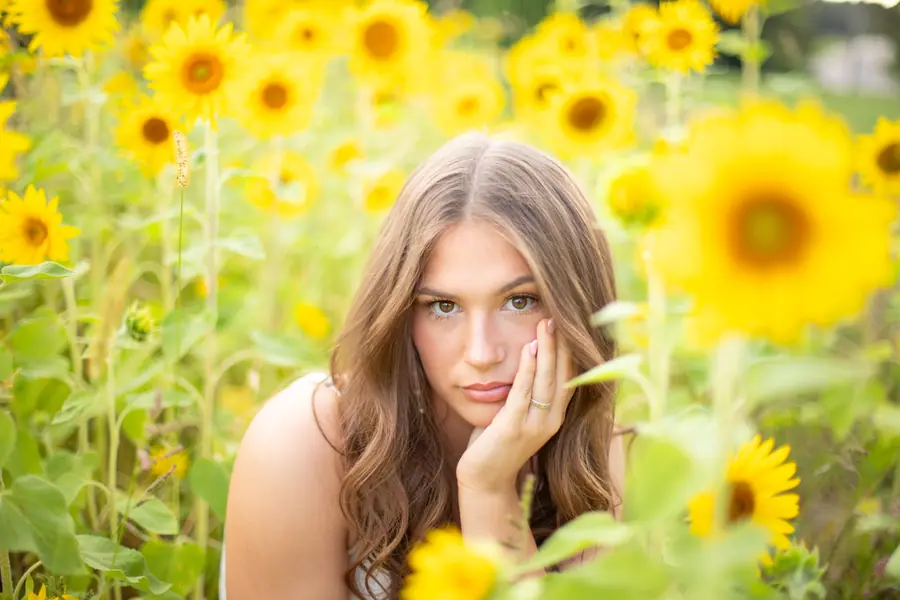 Hand to her cheek among the flowers, the field going soft behind her