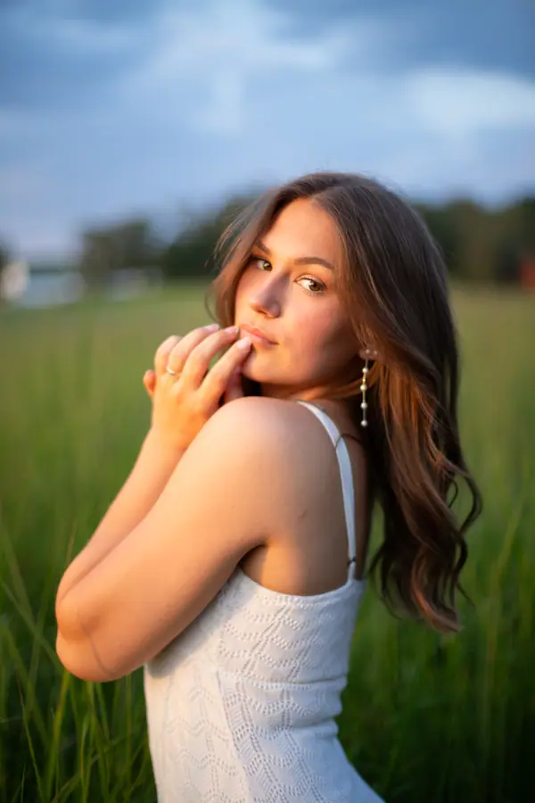 Hands to her face on the gravel track, the meadow grasses lit from behind