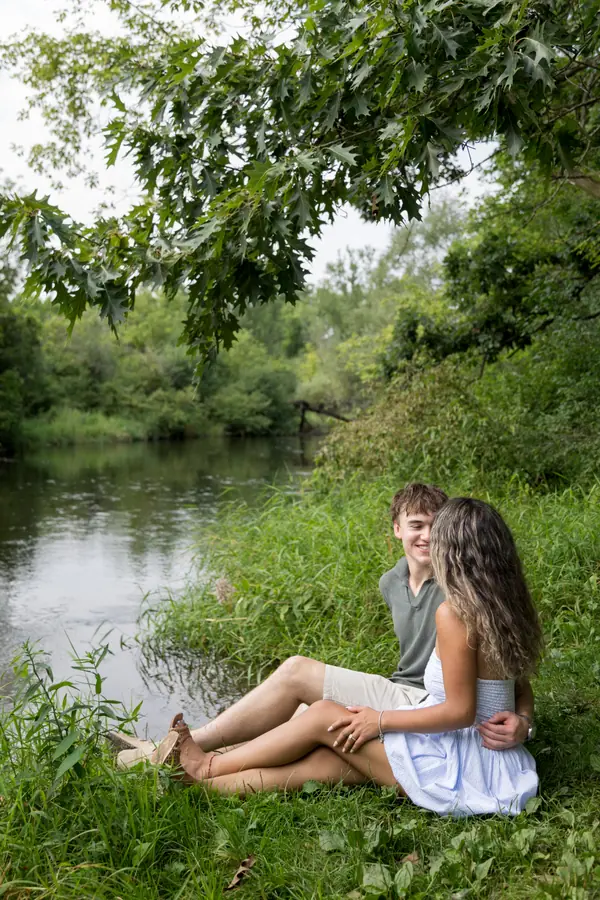 Sitting together on the bank of a slow green river, feet in the grass