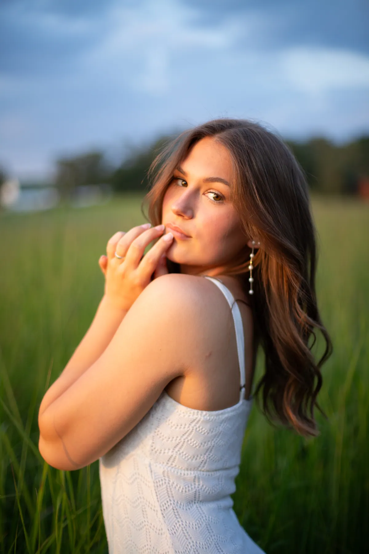 A senior in a white top standing in tall prairie grass in the last of the evening light