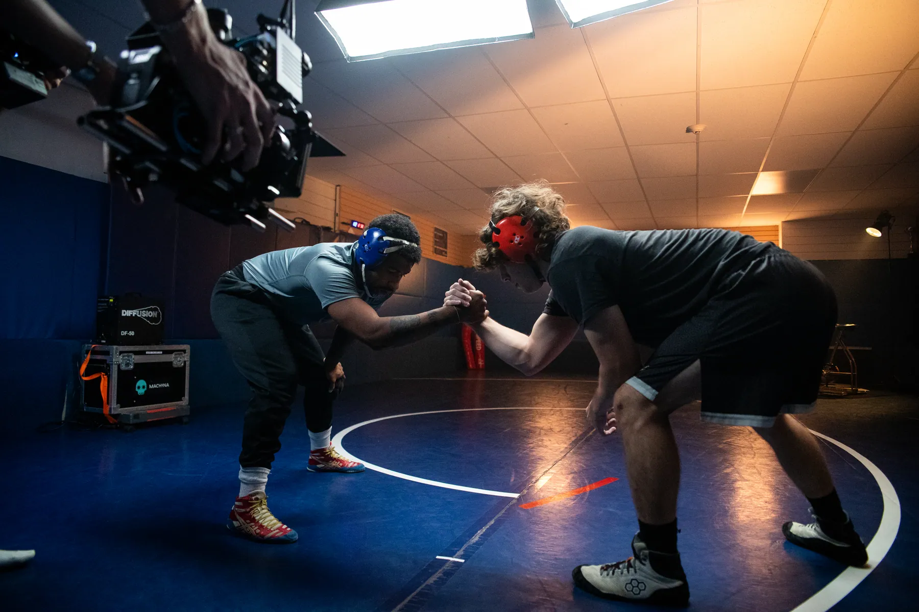 A camera operator low to the floor filming two athletes under studio lights